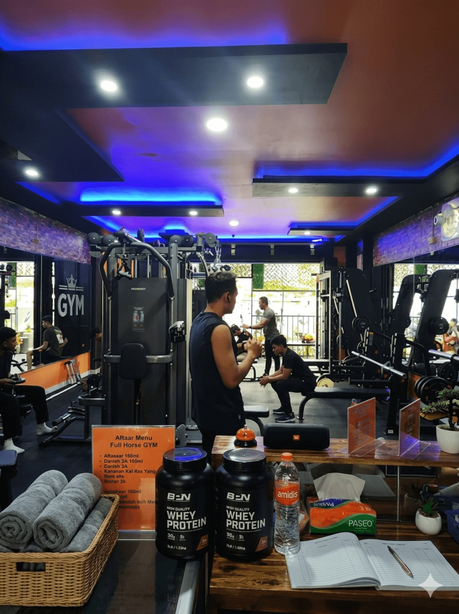 Area dumbbell dan mesin latihan FullHouse GYM dengan pencahayaan biru dan nuansa premium.
